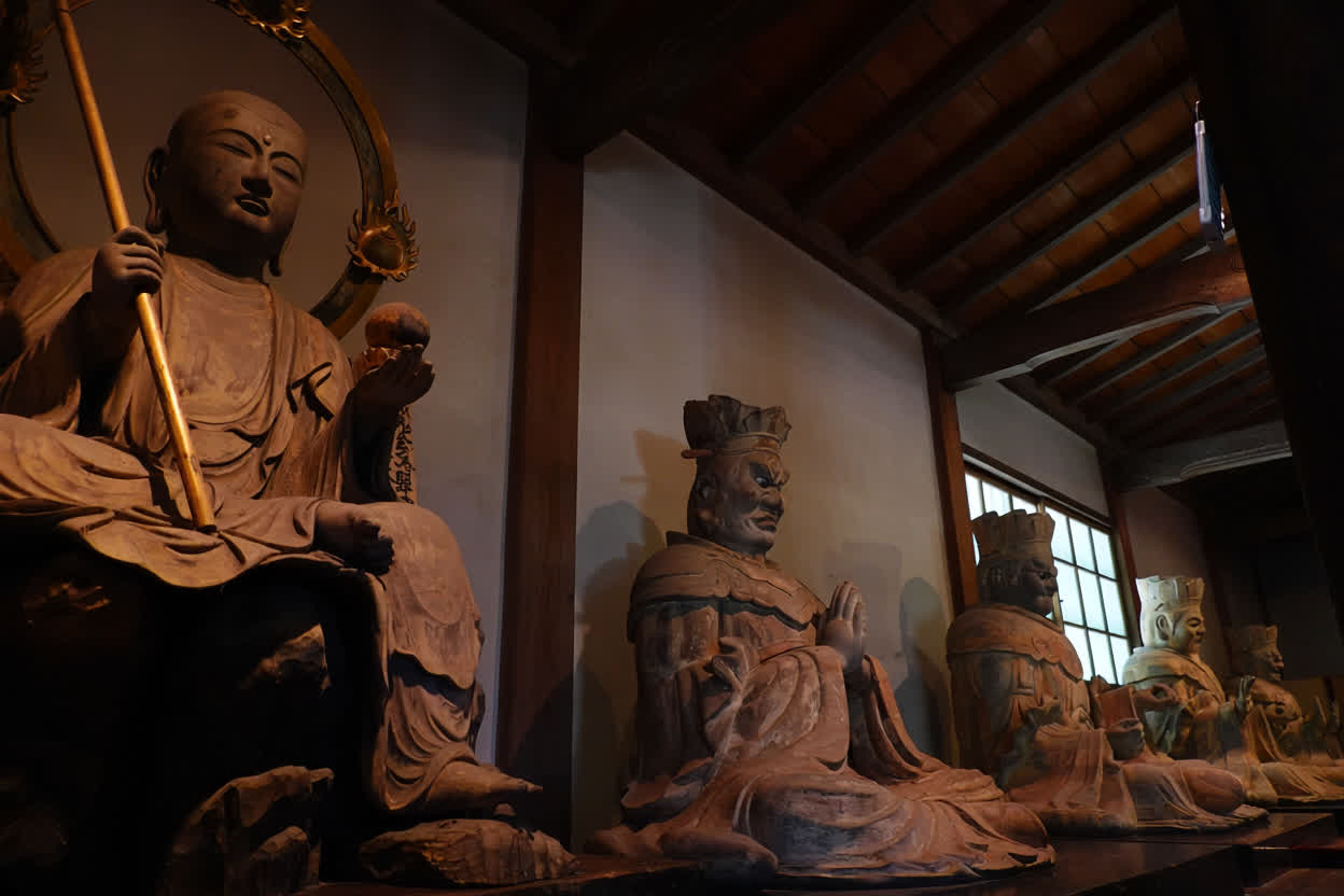 Wooden statues of the Ten Kings of the underworld seated in a dim temple hall, led by Jizō Bosatsu holding a staff